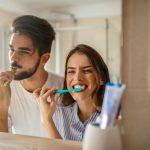 couple brushing teeth in mirror